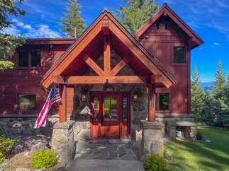 Experience luxury mountain living in this stunning timber-frame home, featuring a grand stone entryway and a welcoming wooden door.