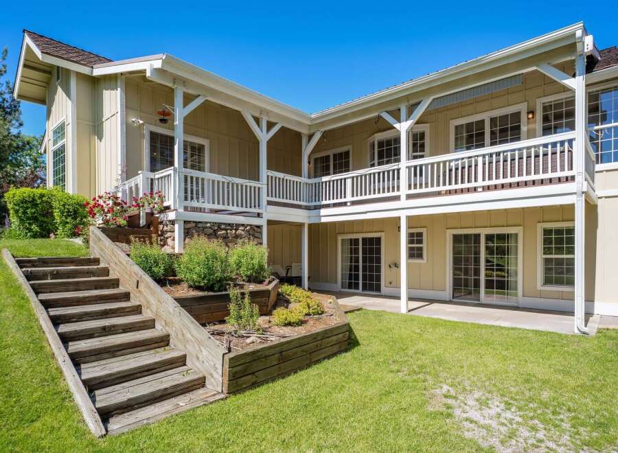 This charming home features a multi-level backyard with wooden stairs leading to a lush green lawn.