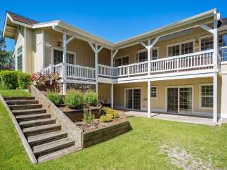 This charming home features a multi-level backyard with wooden stairs leading to a lush green lawn.