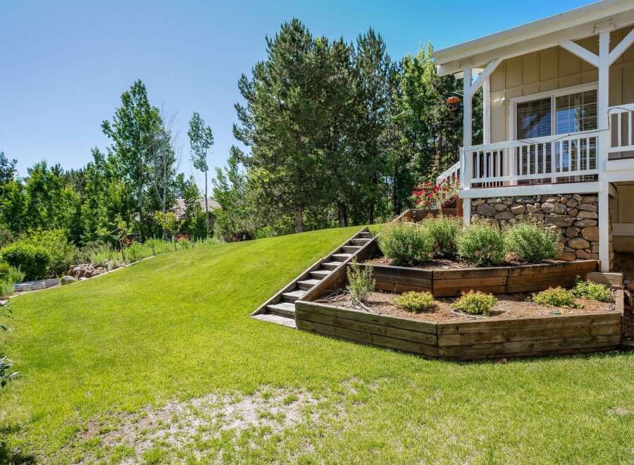 This stunning property features a beautifully landscaped backyard with tiered wooden garden beds and a charming wooden staircase leading up to a covered porch.