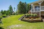 This stunning property features a beautifully landscaped backyard with tiered wooden garden beds and a charming wooden staircase leading up to a covered porch.
