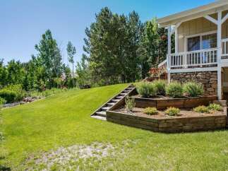 This stunning property features a beautifully landscaped backyard with tiered wooden garden beds and a charming wooden staircase leading up to a covered porch.