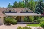 Charming single-family home featuring a welcoming covered porch with a metal roof and decorative white beams, perfect for enjoying the surrounding mature trees and lush landscaping.