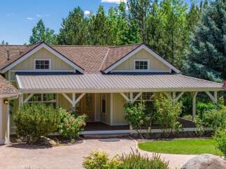 Charming single-family home featuring a welcoming covered porch with a metal roof and decorative white beams, perfect for enjoying the surrounding mature trees and lush landscaping.