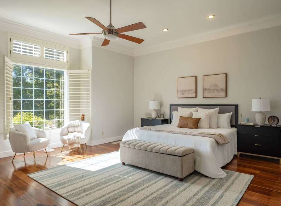 Experience ultimate comfort in this serene bedroom, bathed in natural light from a large bay window with plantation shutters.
