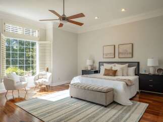 Experience ultimate comfort in this serene bedroom, bathed in natural light from a large bay window with plantation shutters.