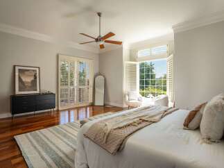 Experience luxurious living in this spacious master bedroom, featuring elegant plantation shutters that open to a serene outdoor view.