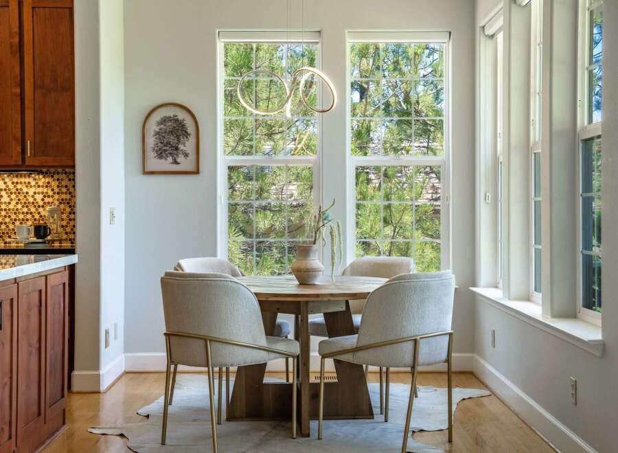 Enjoy meals in this bright dining area, featuring a round wooden table surrounded by four upholstered chairs with gold accents.