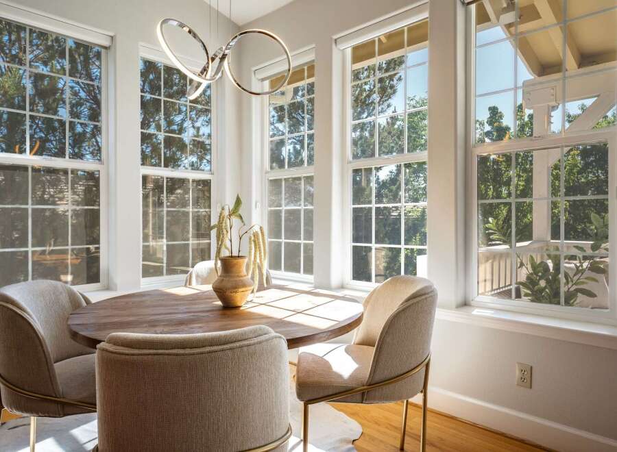 Bathed in natural light, this charming dining area features a round wooden table surrounded by comfortable upholstered chairs.