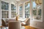 Bathed in natural light, this charming dining area features a round wooden table surrounded by comfortable upholstered chairs.