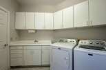 This spacious laundry room features ample white cabinetry for storage, a convenient utility sink, and a built-in paper towel dispenser.