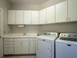 This spacious laundry room features ample white cabinetry for storage, a convenient utility sink, and a built-in paper towel dispenser.