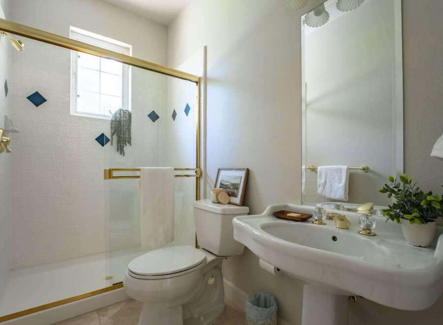 This bright bathroom features a spacious white tiled shower with a gold-trimmed glass door and decorative blue diamond accents.