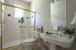 This bright bathroom features a spacious white tiled shower with a gold-trimmed glass door and decorative blue diamond accents.