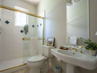 This bright bathroom features a spacious white tiled shower with a gold-trimmed glass door and decorative blue diamond accents.