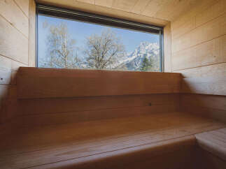 Experience tranquility in this stunning sauna, featuring panoramic views of snow-capped mountains and lush trees.