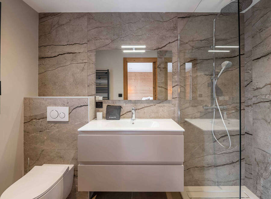 This modern bathroom showcases a sleek design with its marble-effect tiled walls and a frameless glass shower enclosure.