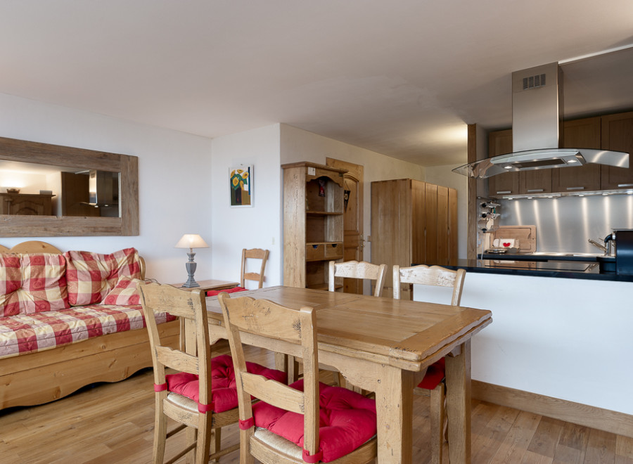 Cozy chalet apartment featuring a rustic wooden dining table with red cushions, a comfortable checkered sofa, and a fully equipped kitchen with modern appliances.