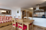 Cozy chalet apartment featuring a rustic wooden dining table with red cushions, a comfortable checkered sofa, and a fully equipped kitchen with modern appliances.