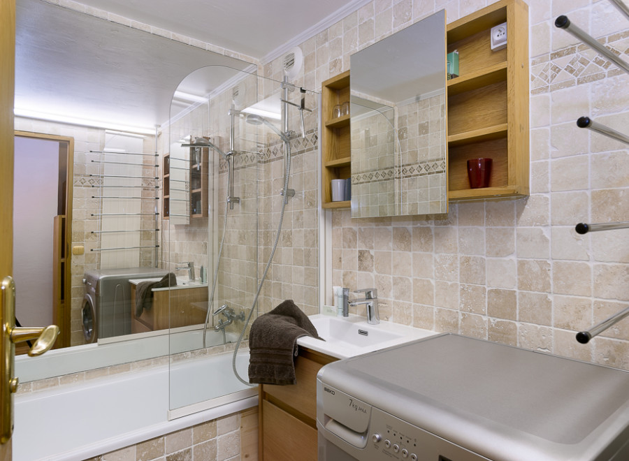 This charming bathroom boasts a modern aesthetic with beige tile, a glass-enclosed shower, and a built-in vanity with a washing machine.