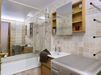 This charming bathroom boasts a modern aesthetic with beige tile, a glass-enclosed shower, and a built-in vanity with a washing machine.