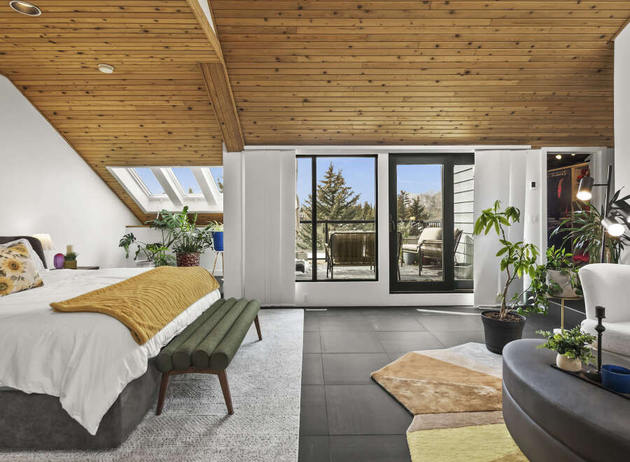 This stunning bedroom boasts a unique design with a wooden slatted ceiling and large windows that offer breathtaking views.