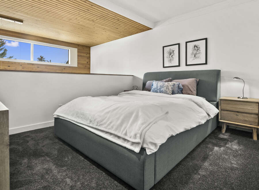 This modern bedroom boasts a cozy ambiance with its plush gray carpet and a comfortable bed.