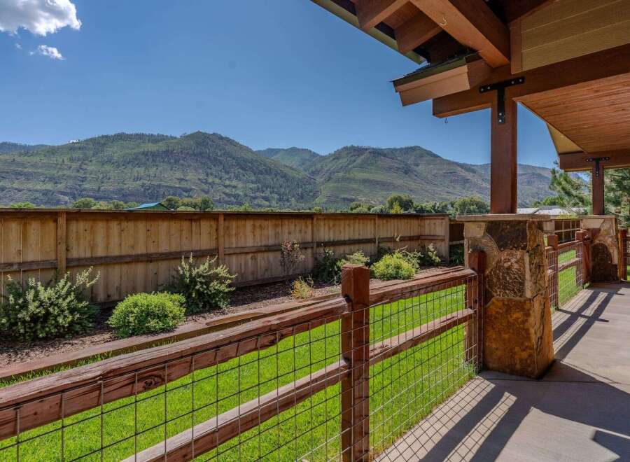 Enjoy breathtaking mountain views from this stunning property, featuring a spacious backyard with a wooden fence and lush green lawn.