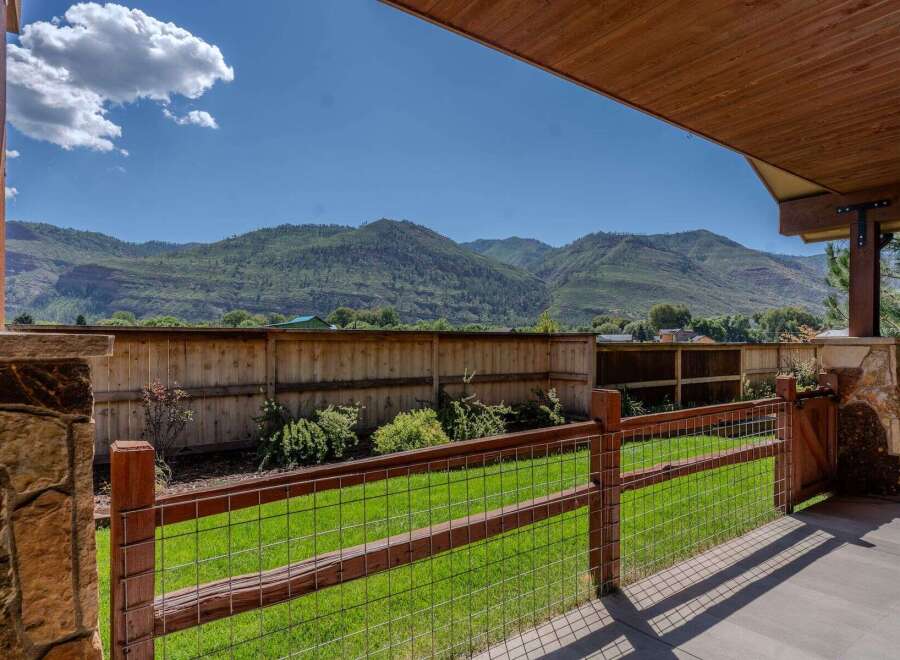 Experience breathtaking mountain views from this stunning property, framed by a rustic wooden fence and a covered patio.