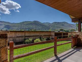 Experience breathtaking mountain views from this stunning property, framed by a rustic wooden fence and a covered patio.