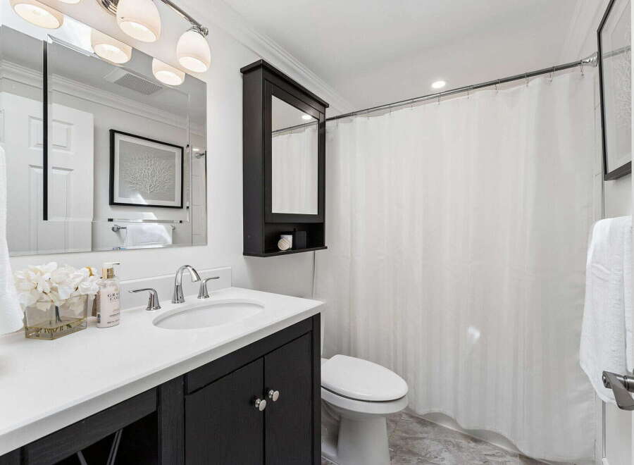 This modern bathroom features a sleek vanity with a white countertop and dark cabinetry, offering ample storage and a stylish contrast.