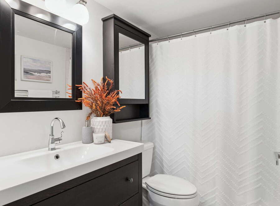 This modern bathroom features a sleek vanity with a dark wood finish, complemented by a stylish mirror and a decorative plant.
