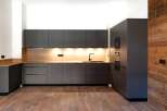 This modern kitchen boasts sleek, dark gray cabinetry complemented by a warm wood backsplash and flooring, creating a stylish and inviting space.
