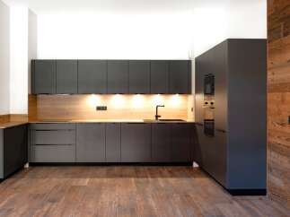 This modern kitchen boasts sleek, dark gray cabinetry complemented by a warm wood backsplash and flooring, creating a stylish and inviting space.