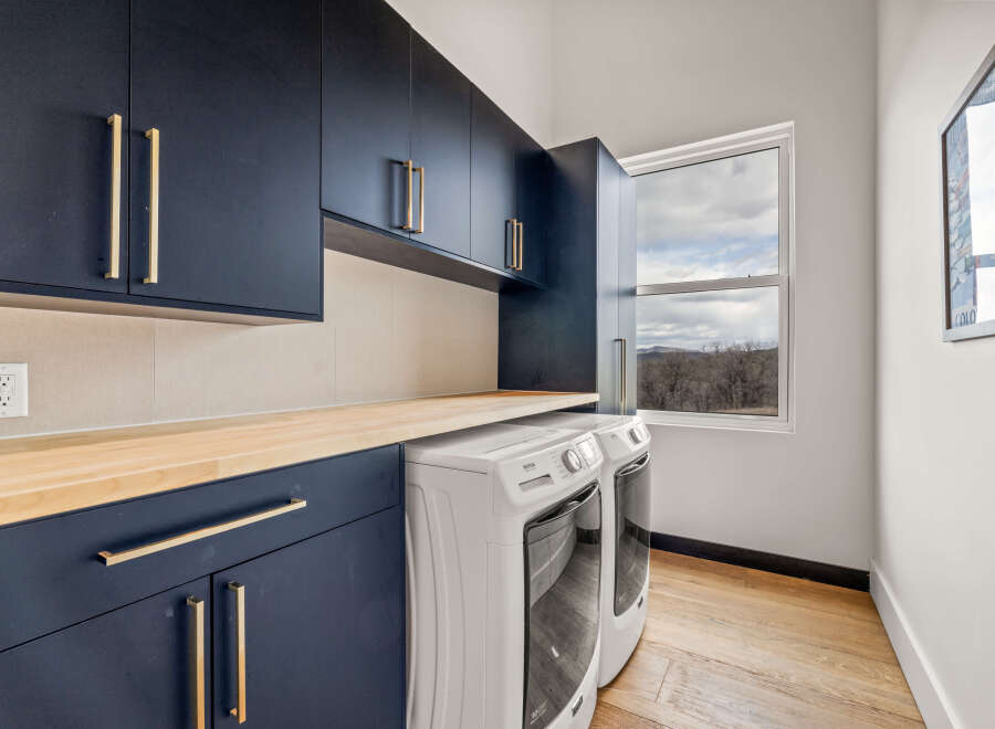 This stunning laundry room boasts modern design with navy blue cabinetry and sleek gold hardware.