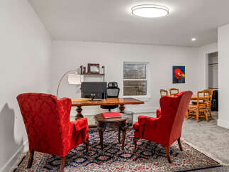 Step into this elegant home office, featuring a spacious wooden desk and two plush red armchairs, perfect for focused work or client meetings.