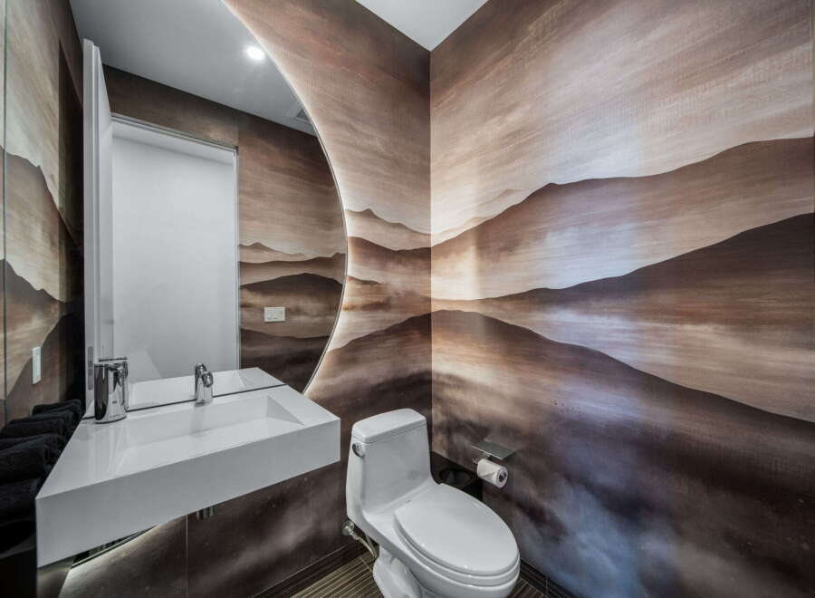 This stunning powder room showcases a unique artistic flair with its custom mountain mural wallpaper.