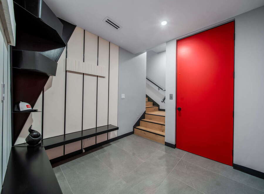 This modern entryway showcases a striking red door and a unique black staircase.