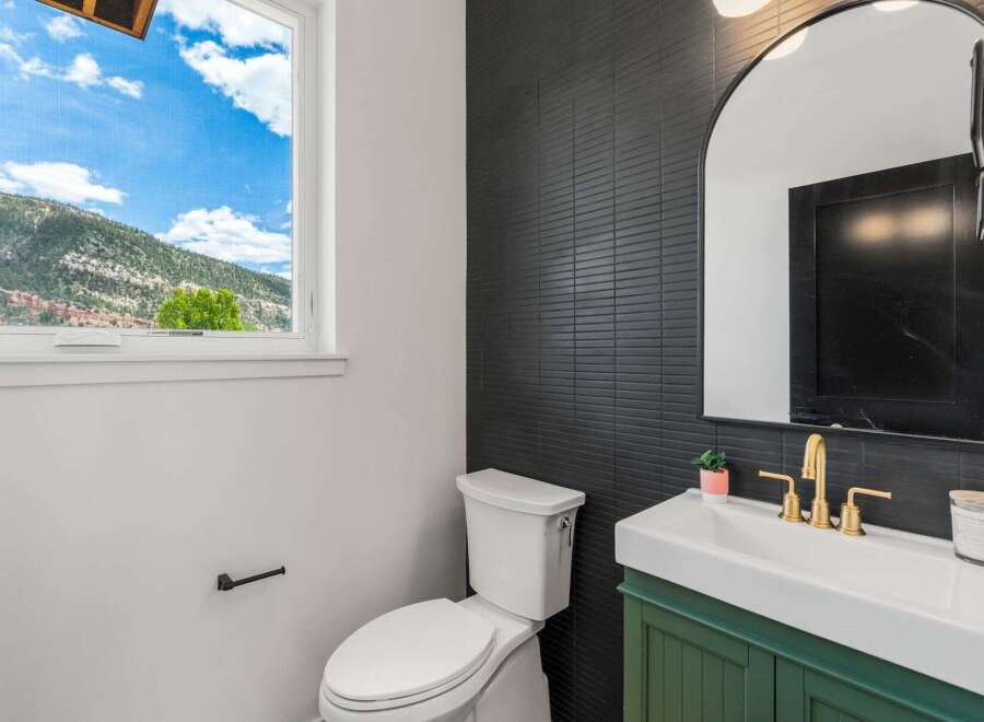 This stunning bathroom features a modern design with a sleek black tiled wall and a stylish green vanity.