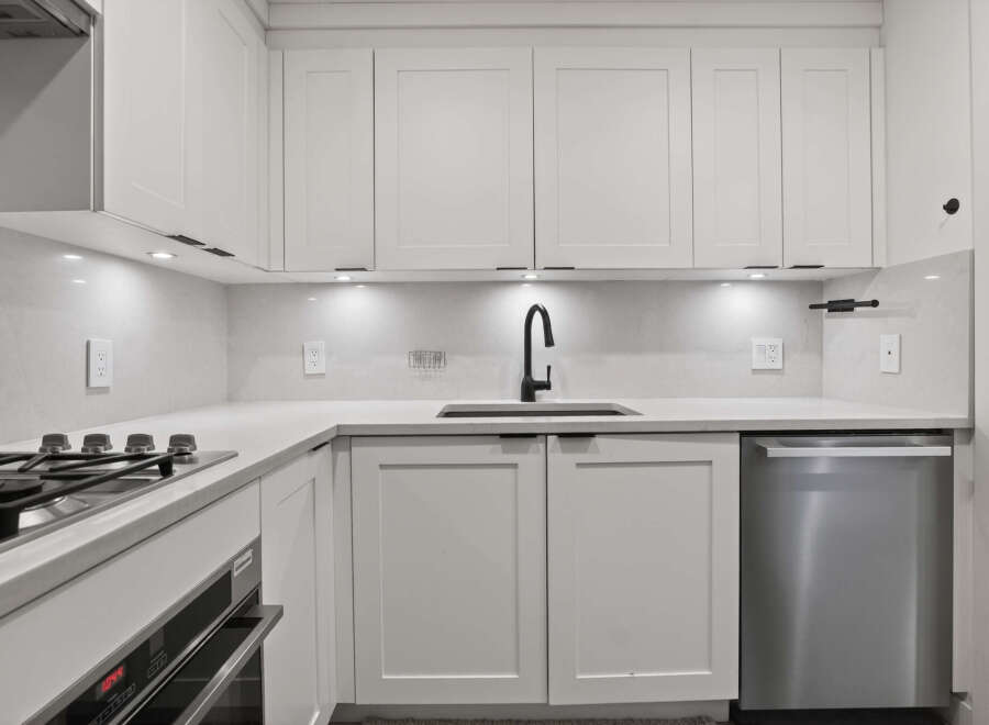 This modern kitchen boasts sleek white cabinetry, a stainless steel dishwasher, and a stylish black faucet.