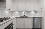 This modern kitchen boasts sleek white cabinetry, a stainless steel dishwasher, and a stylish black faucet.
