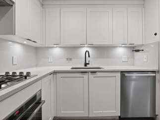 This modern kitchen boasts sleek white cabinetry, a stainless steel dishwasher, and a stylish black faucet.
