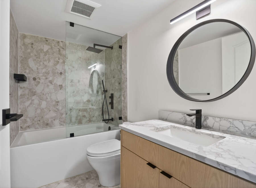 Step into a modern bathroom oasis! This stunning space features a sleek, round mirror and a stylish vanity with a marble countertop.