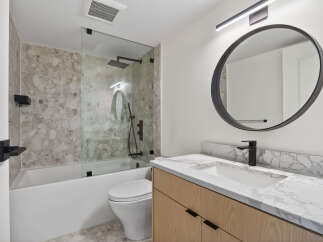 Step into a modern bathroom oasis! This stunning space features a sleek, round mirror and a stylish vanity with a marble countertop.