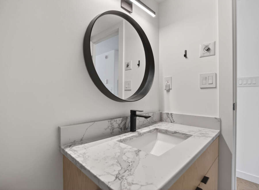 This modern bathroom features a sleek, round mirror and a stylish black faucet.
