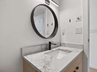 This modern bathroom features a sleek, round mirror and a stylish black faucet.