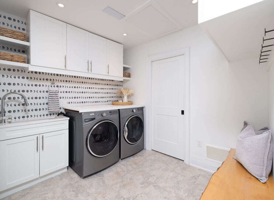 This stunning laundry room boasts a modern design with sleek white cabinetry and a unique moon phase backsplash.