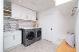 This stunning laundry room boasts a modern design with sleek white cabinetry and a unique moon phase backsplash.