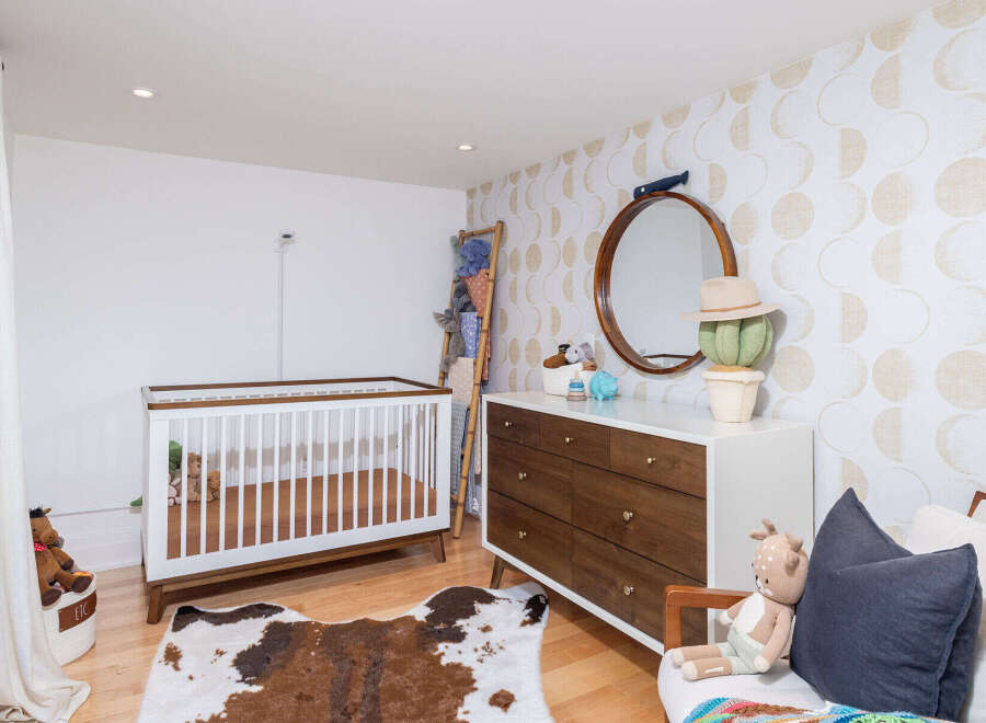 This charming nursery features a modern crib with a wooden frame, complemented by a stylish dresser and a unique cowhide rug.