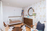 This charming nursery features a modern crib with a wooden frame, complemented by a stylish dresser and a unique cowhide rug.